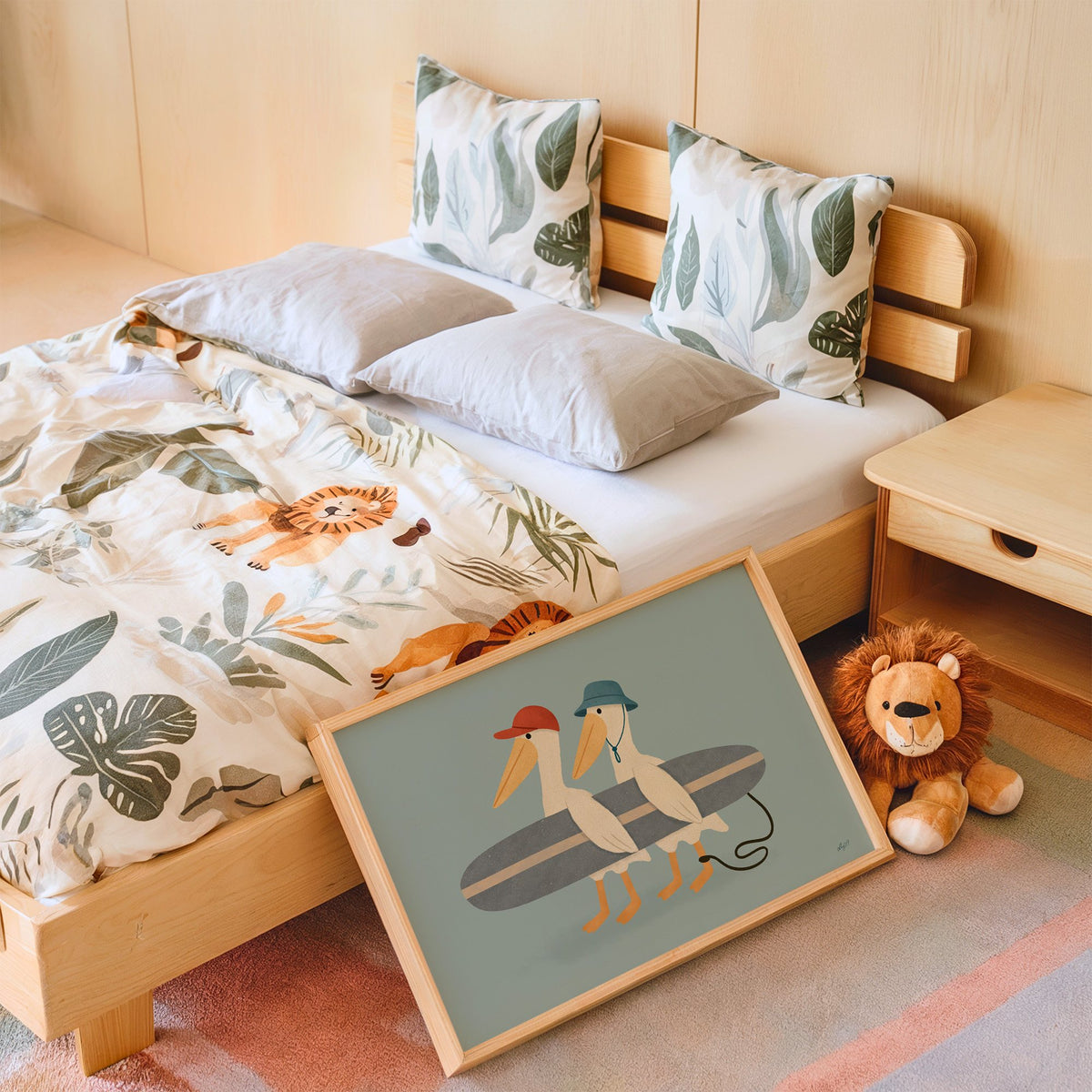 Two pelicans carrying surfboard nursery print in an oak frame leaning on a kids bed by a lion plush