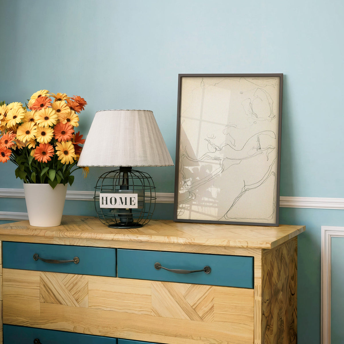 Pencil contour sketch of an abstract profile print in a charcoal frame on a teal dresser beside orange and yellow daisies