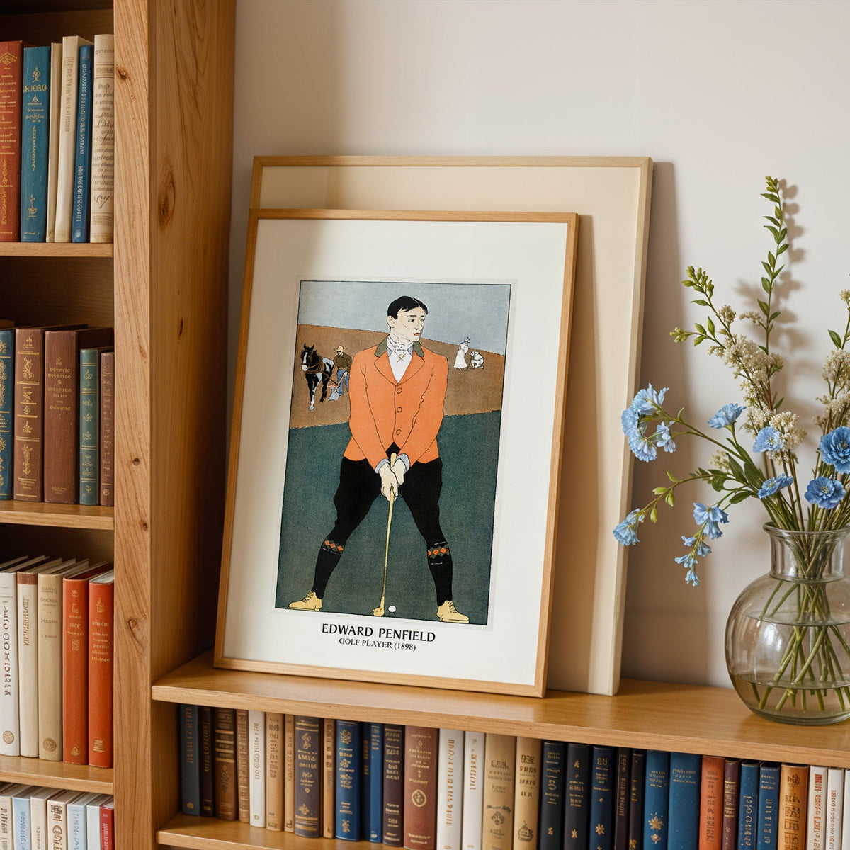 Penfield poster in an oak frame leaning on a bookshelf beside blue flowers