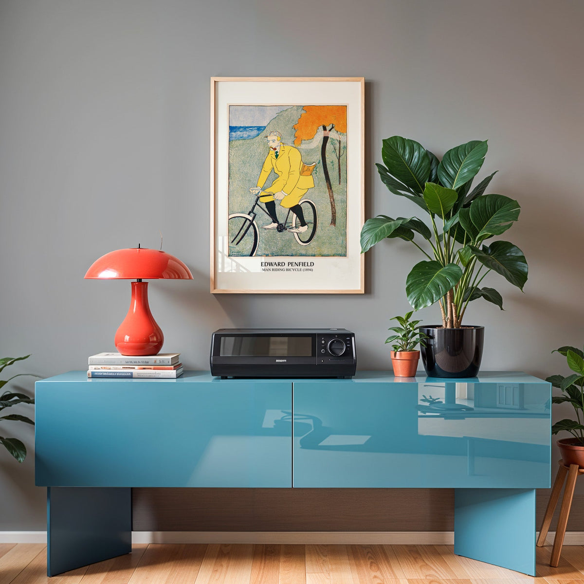 Penfield bicycle print in an oak frame above a teal sideboard with a red lamp
