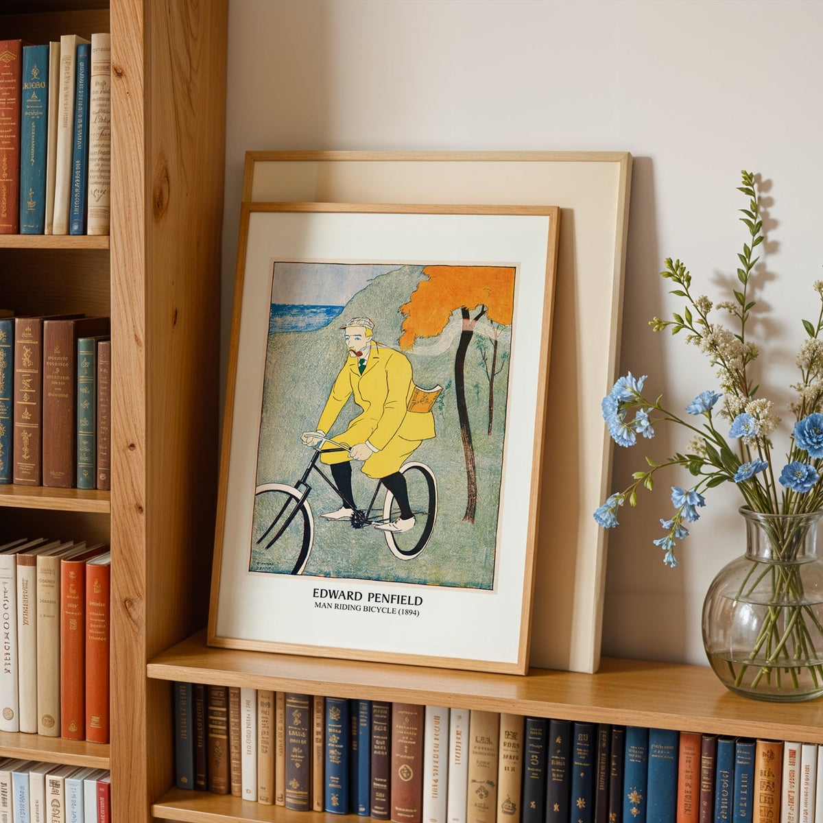 Bicycle print in an oak frame leaning on a bookshelf beside blue flowers