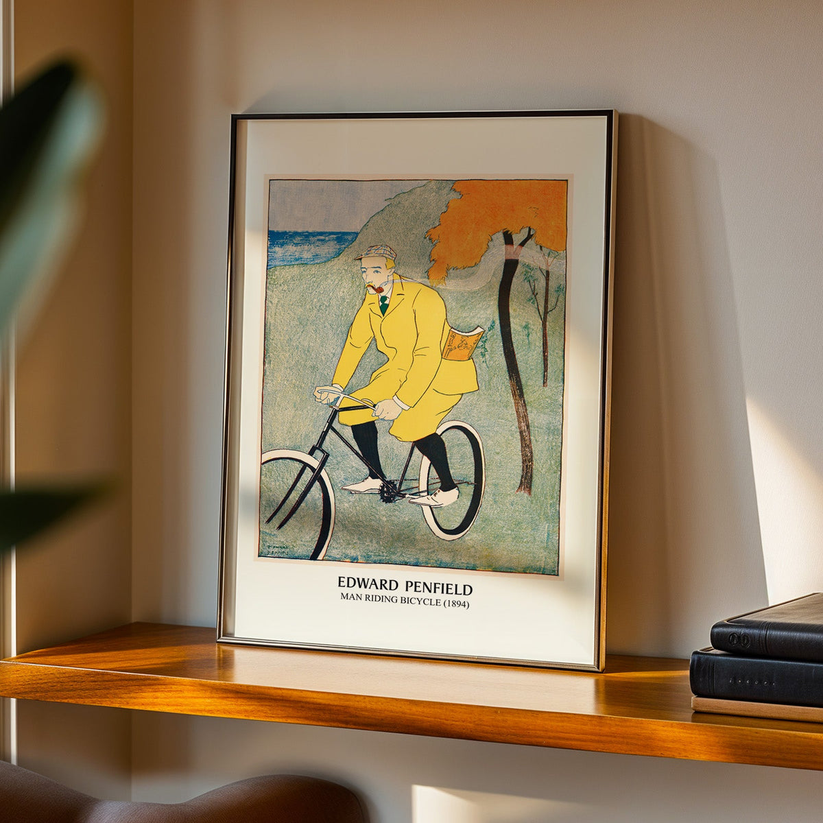 Man Riding Bicycle print in a black frame on a walnut shelf in evening light