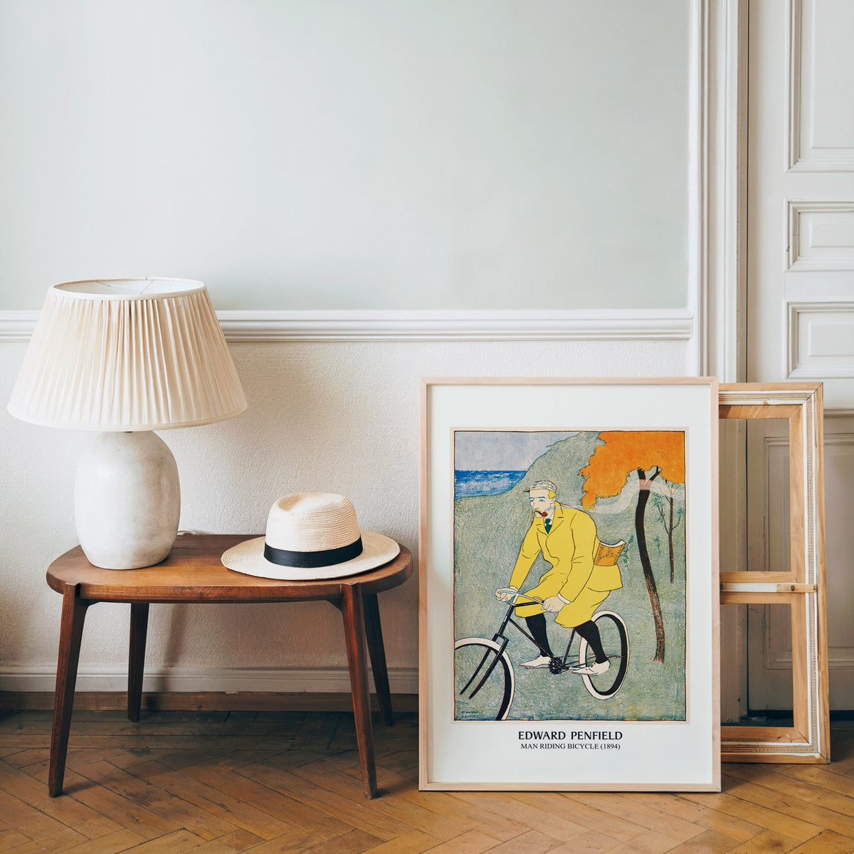 Retro bicycle poster in a light wood frame leaning by a bench and panama hat