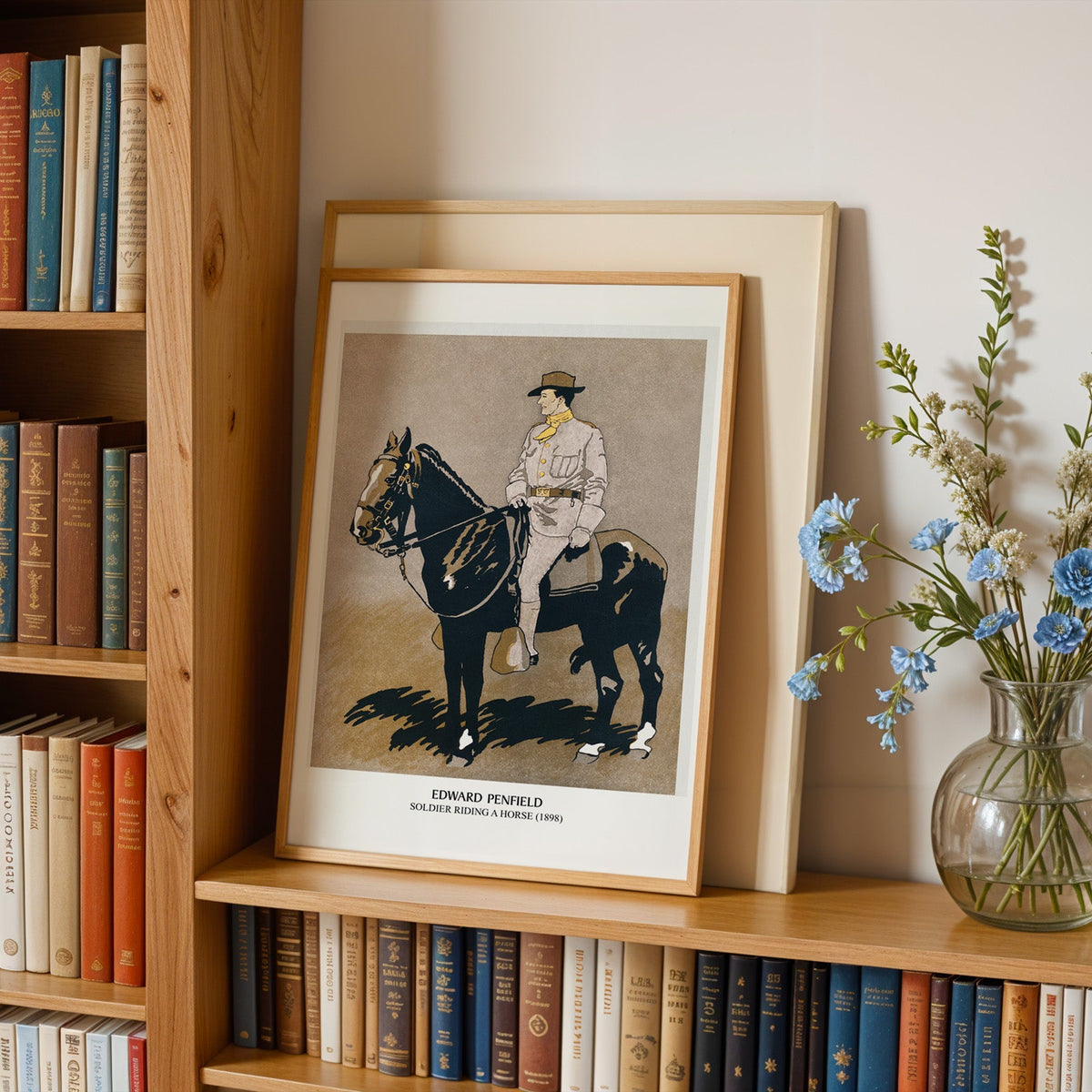 Penfield poster in an oak frame leaning on a bookshelf beside blue flowers