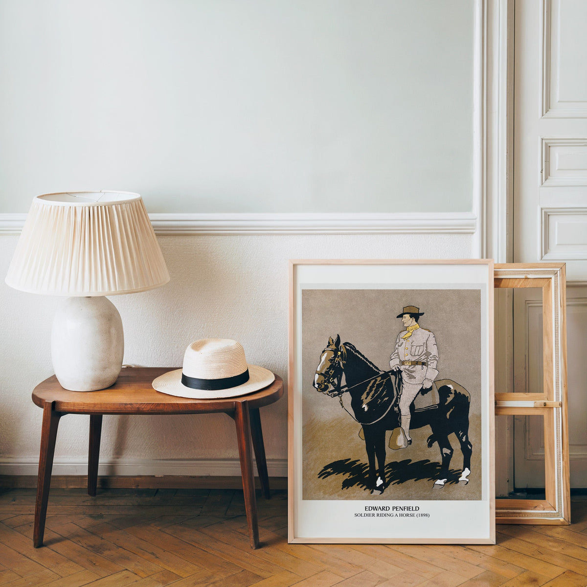 Vintage cavalry poster in a light wood frame leaning by a bench and panama hat