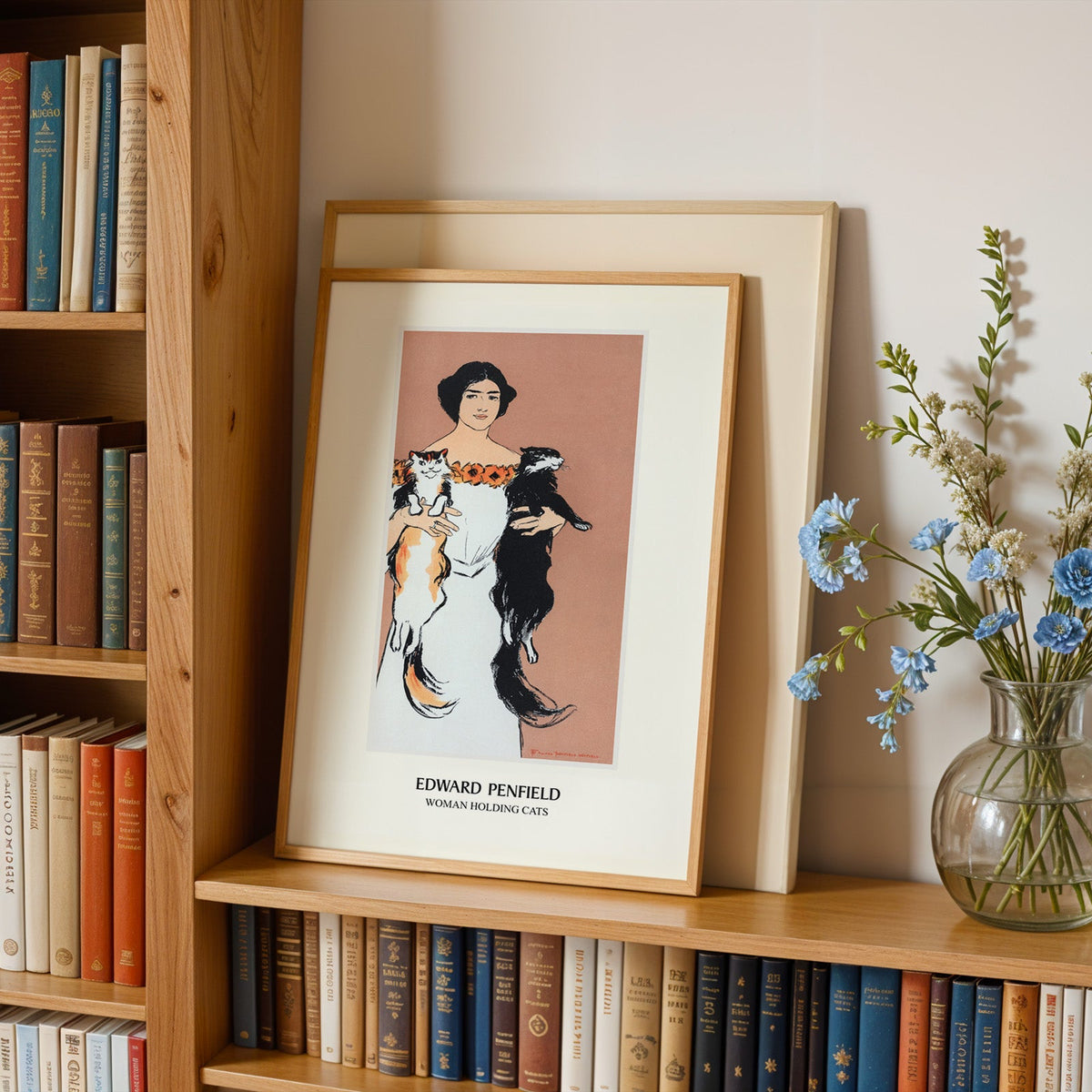 Cat print in an oak frame leaning on a bookshelf beside blue flowers