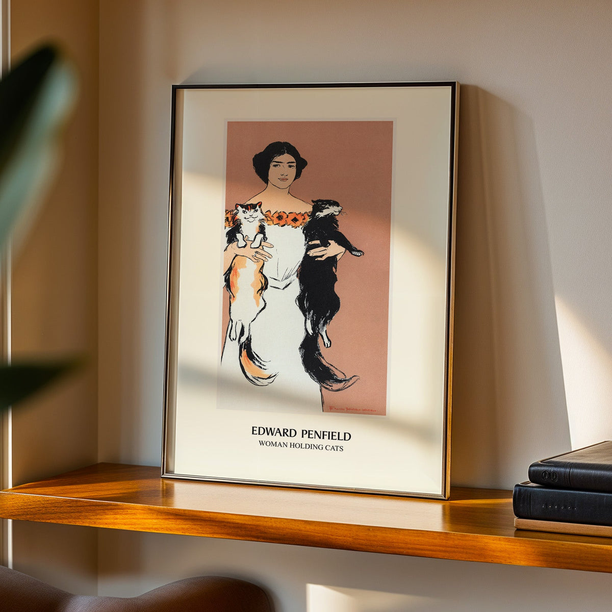 Woman Holding Cats print in a black frame on a walnut shelf in evening light