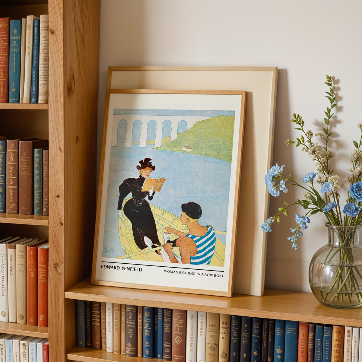 Row boat print in an oak frame leaning on a bookshelf beside blue flowers