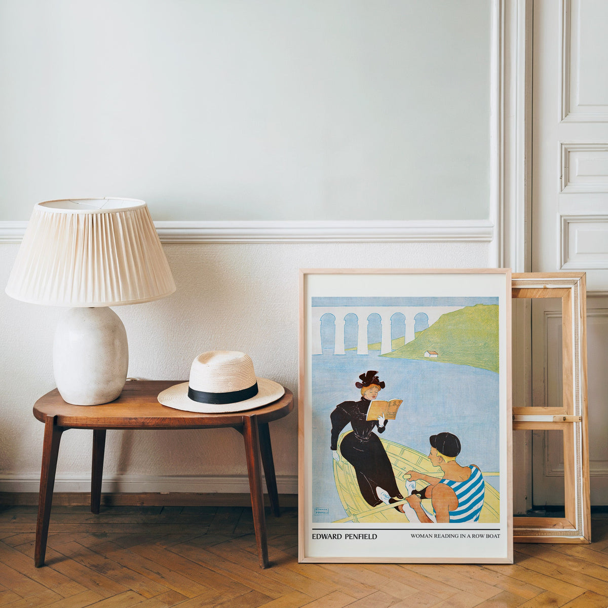 Penfield summer poster in a light wood frame leaning by a bench and panama hat