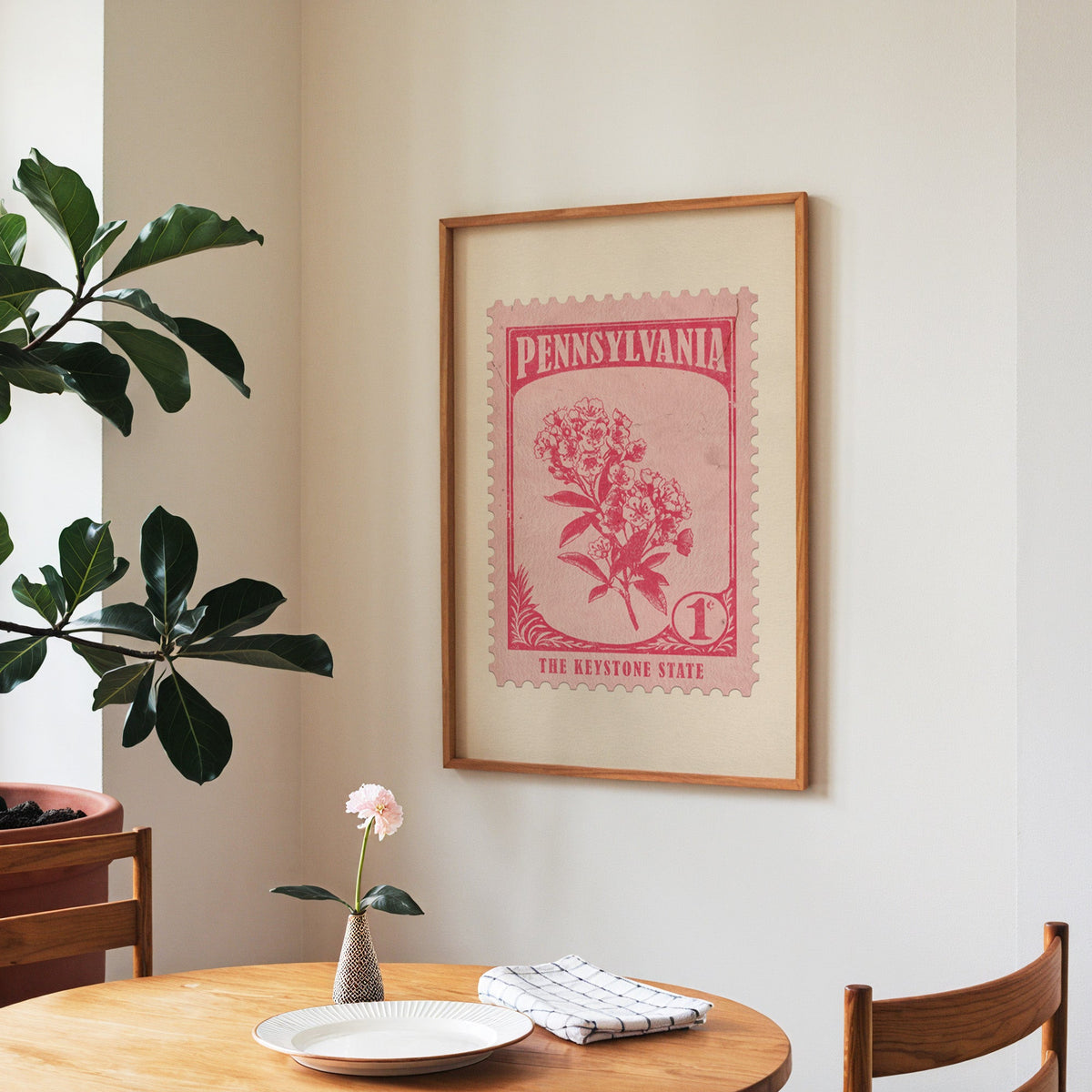 Pennsylvania state flower print framed above a round wooden table with a single bloom in a vase and books