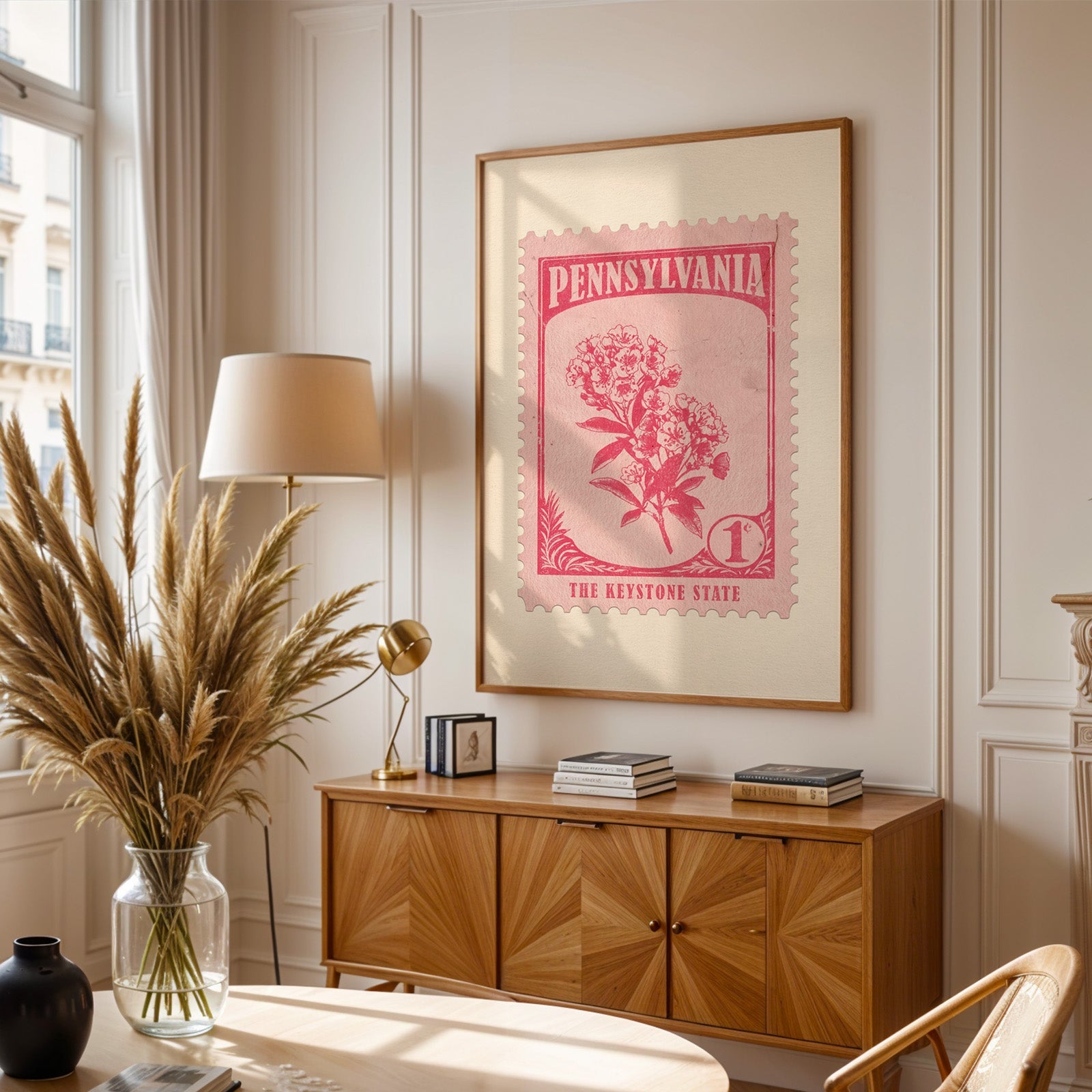 Pennsylvania stamp print framed above a wooden sideboard, pampas grass in a glass vase and a floor lamp