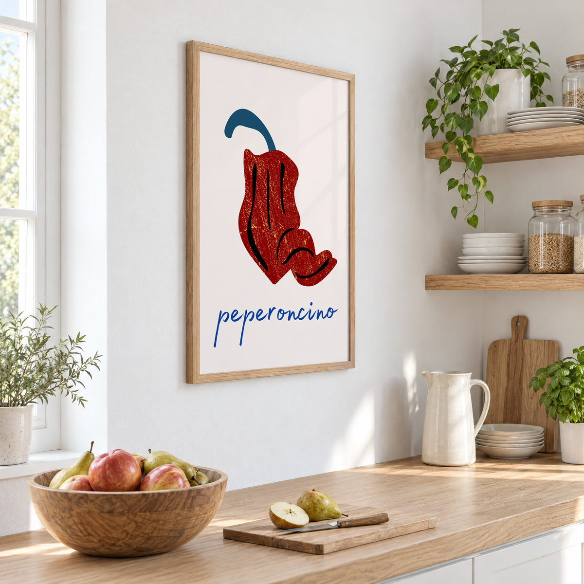 peperoncino red chili grunge print in an oak frame on a white kitchen wall above a counter with apples and pears, seen at an angle