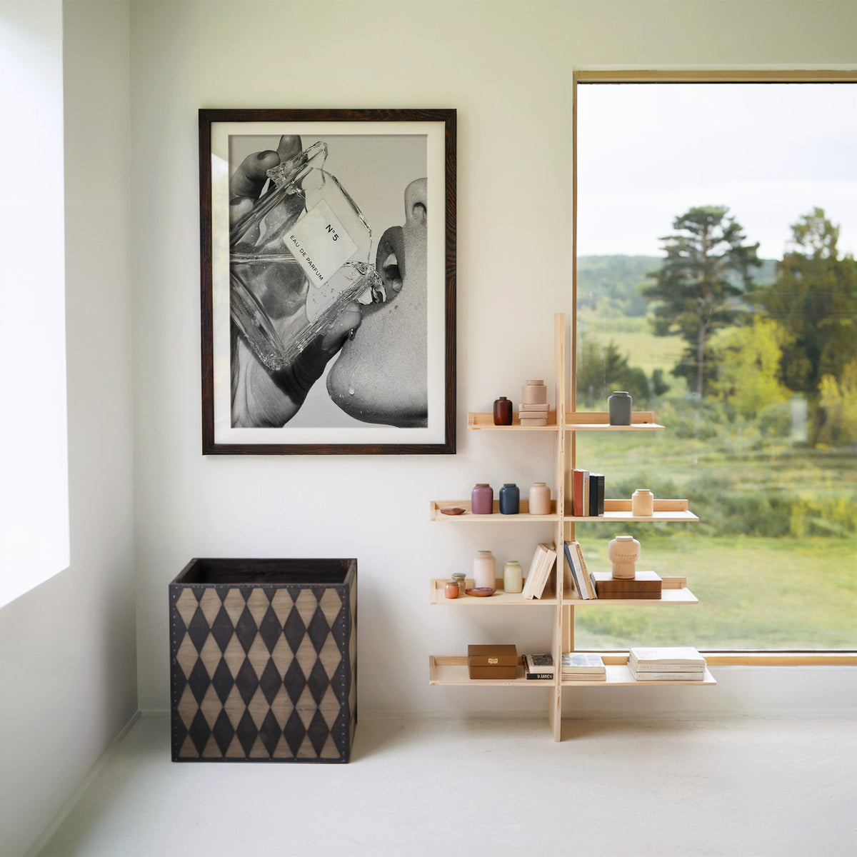 Cut-glass perfume bottle at a woman's lips print in a walnut frame with a white mat beside wooden shelves and a garden window