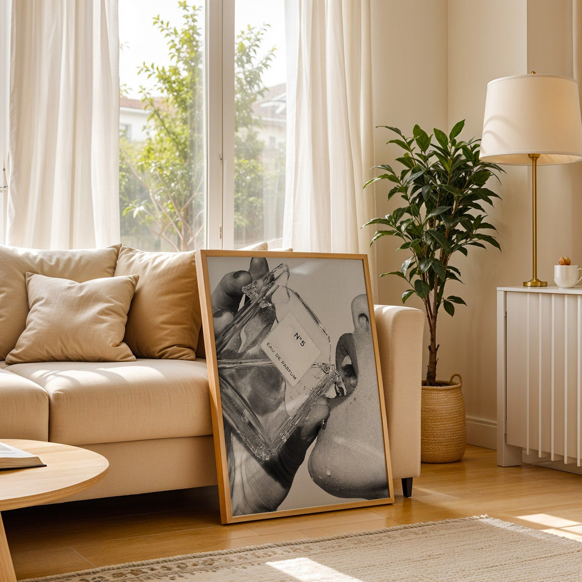 Cut-glass perfume bottle at a woman's lips print in a light oak frame leaning on a cream sofa beside a floor lamp