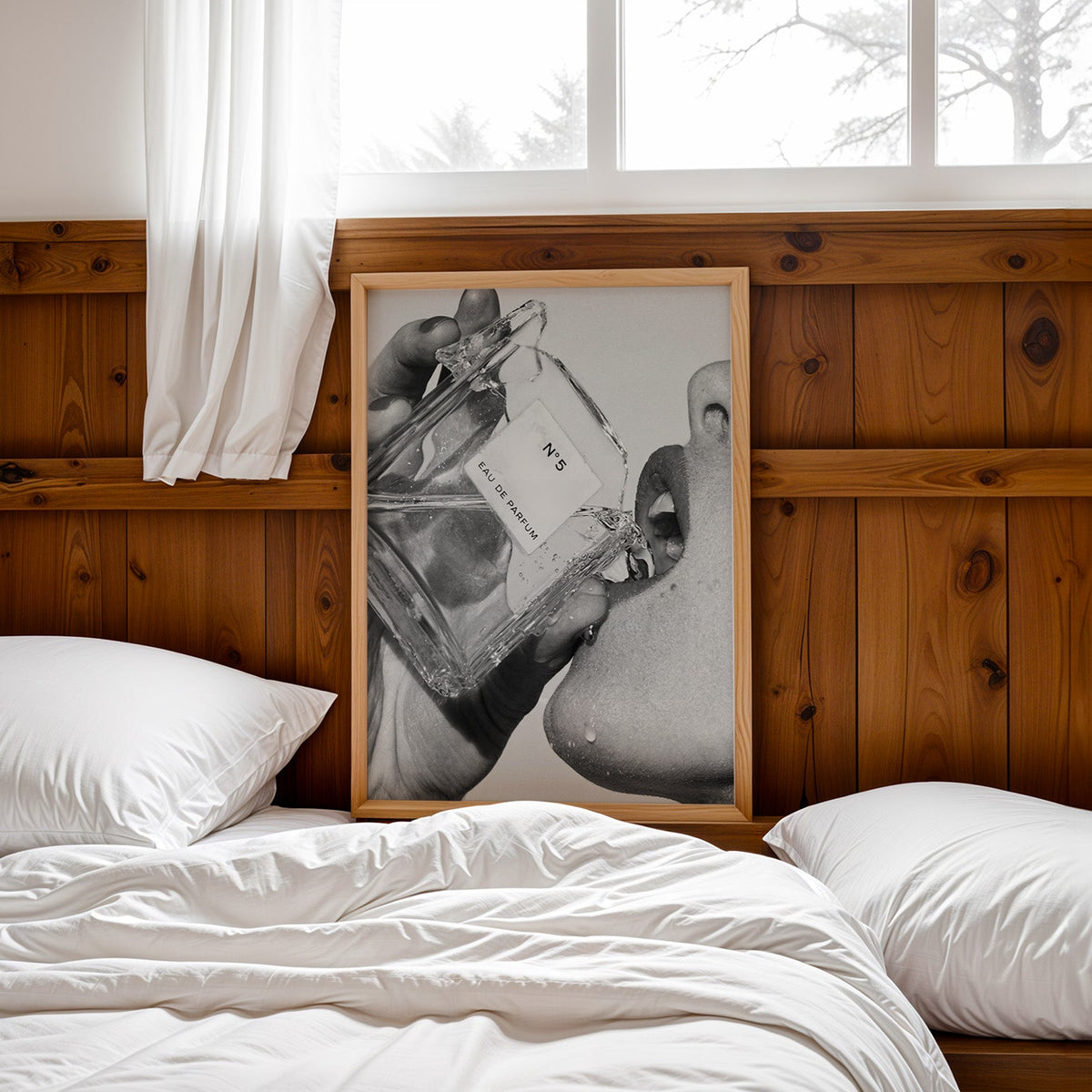 Cut-glass perfume bottle at a woman's lips print in a pine frame leaning on a wood headboard over white bedding