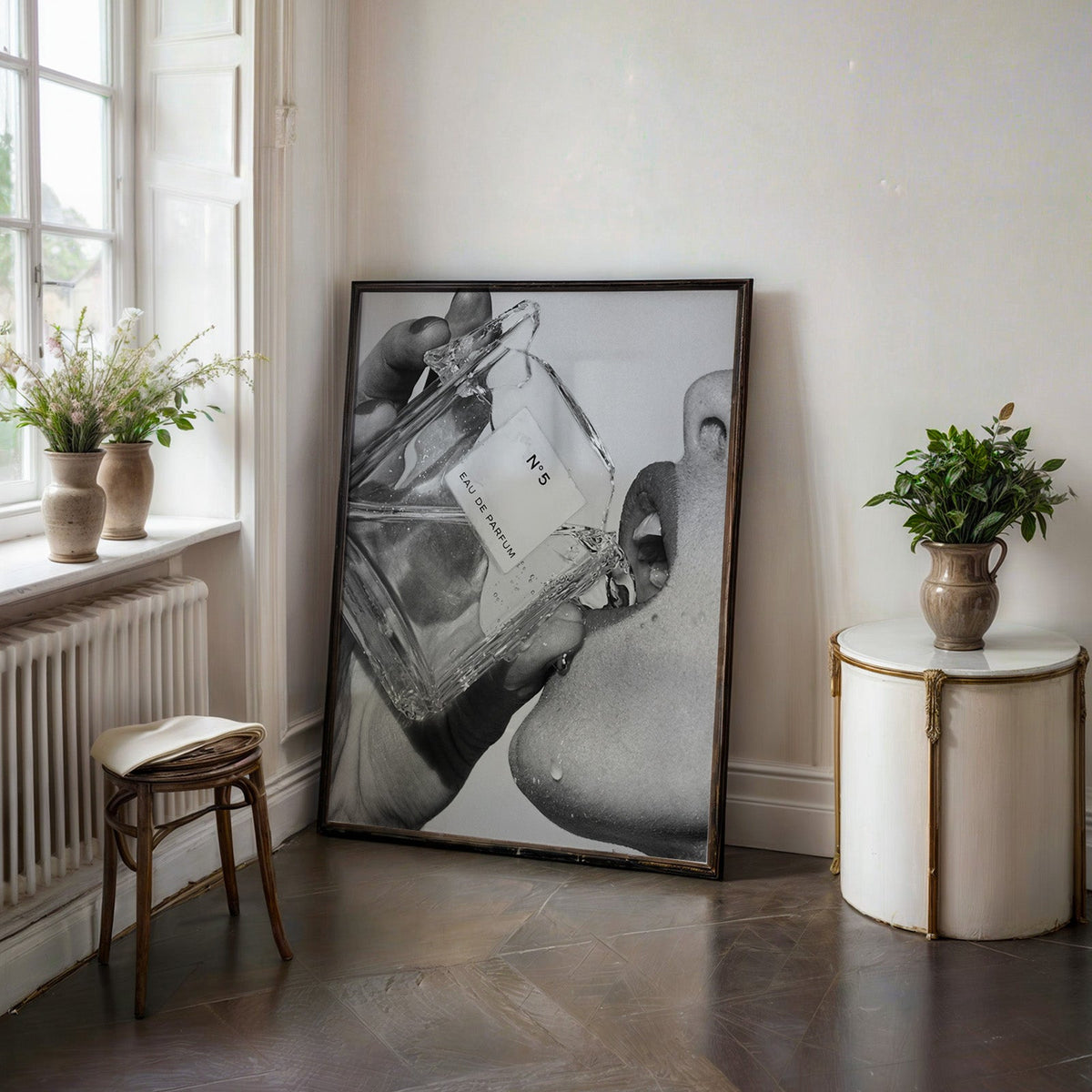 Cut-glass perfume bottle at a woman's lips print in a black frame on a dark stone floor beside a white side table