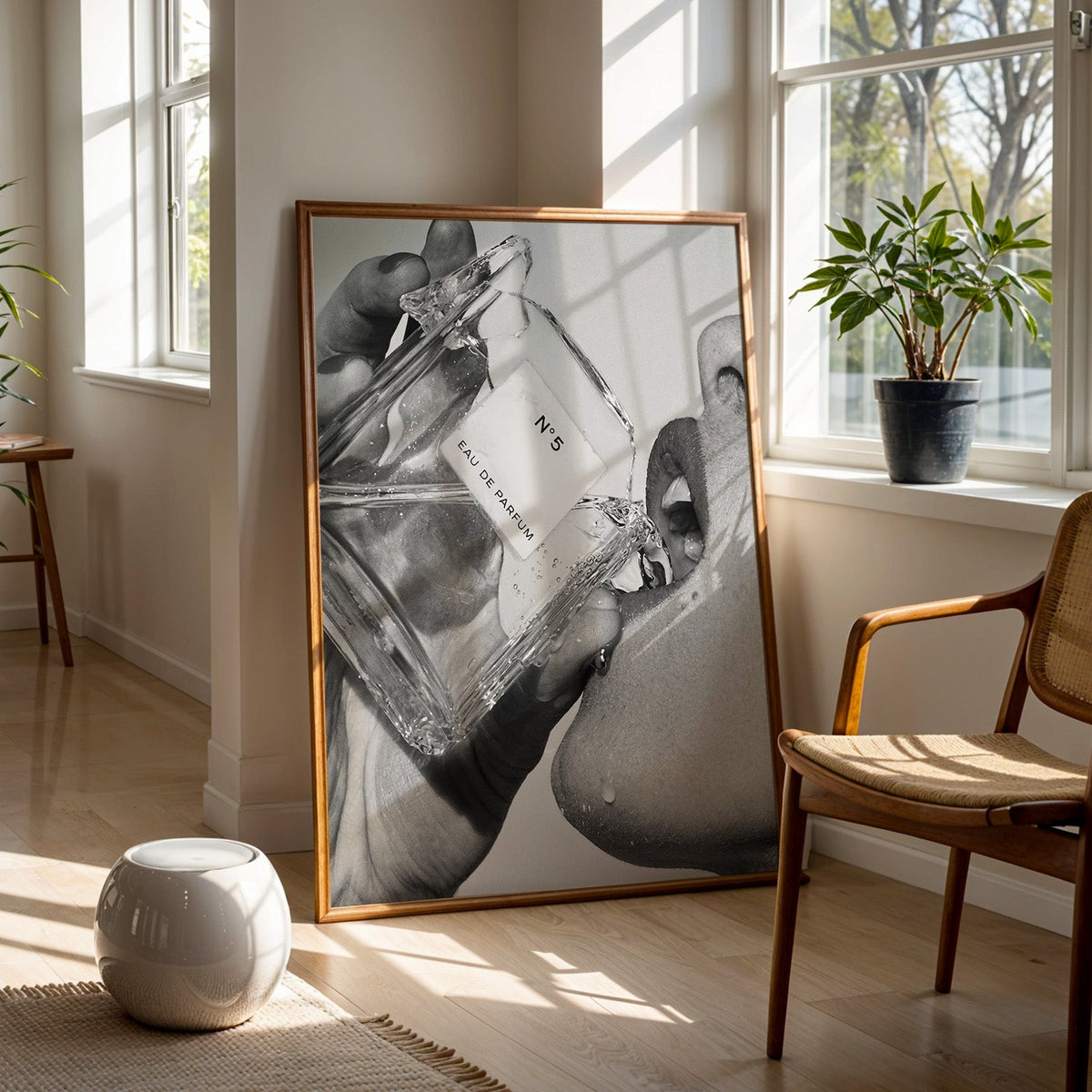 Cut-glass perfume bottle at a woman's lips print in a walnut frame on a wood floor beside a cane chair and sunny window