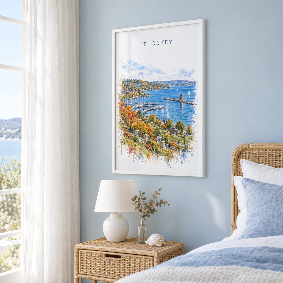 Petoskey watercolor print in a white frame on a pale blue wall beside a rattan bed in a coastal bedroom