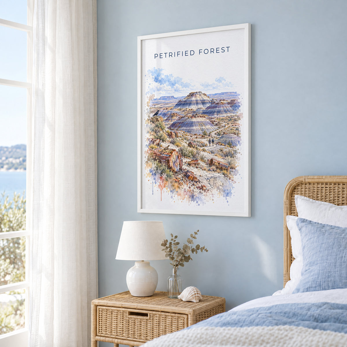 Petrified Forest National Park watercolor print in a white frame on a pale blue wall beside a rattan bed in a coastal bedroom