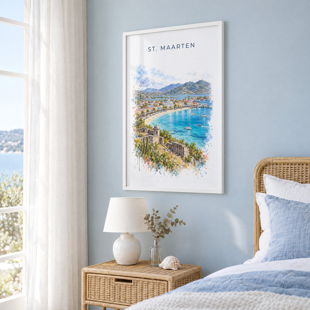 St. Maarten watercolor print in a white frame on a pale blue wall beside a rattan bed in a coastal bedroom