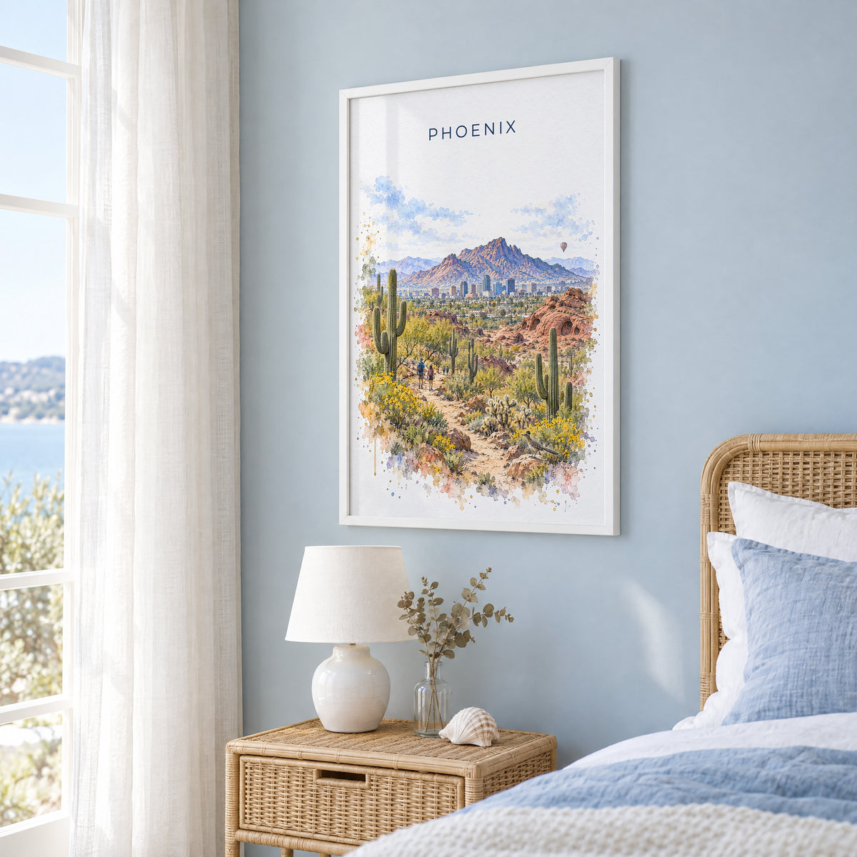 Phoenix watercolor print in a white frame on a pale blue wall beside a rattan bed in a coastal bedroom