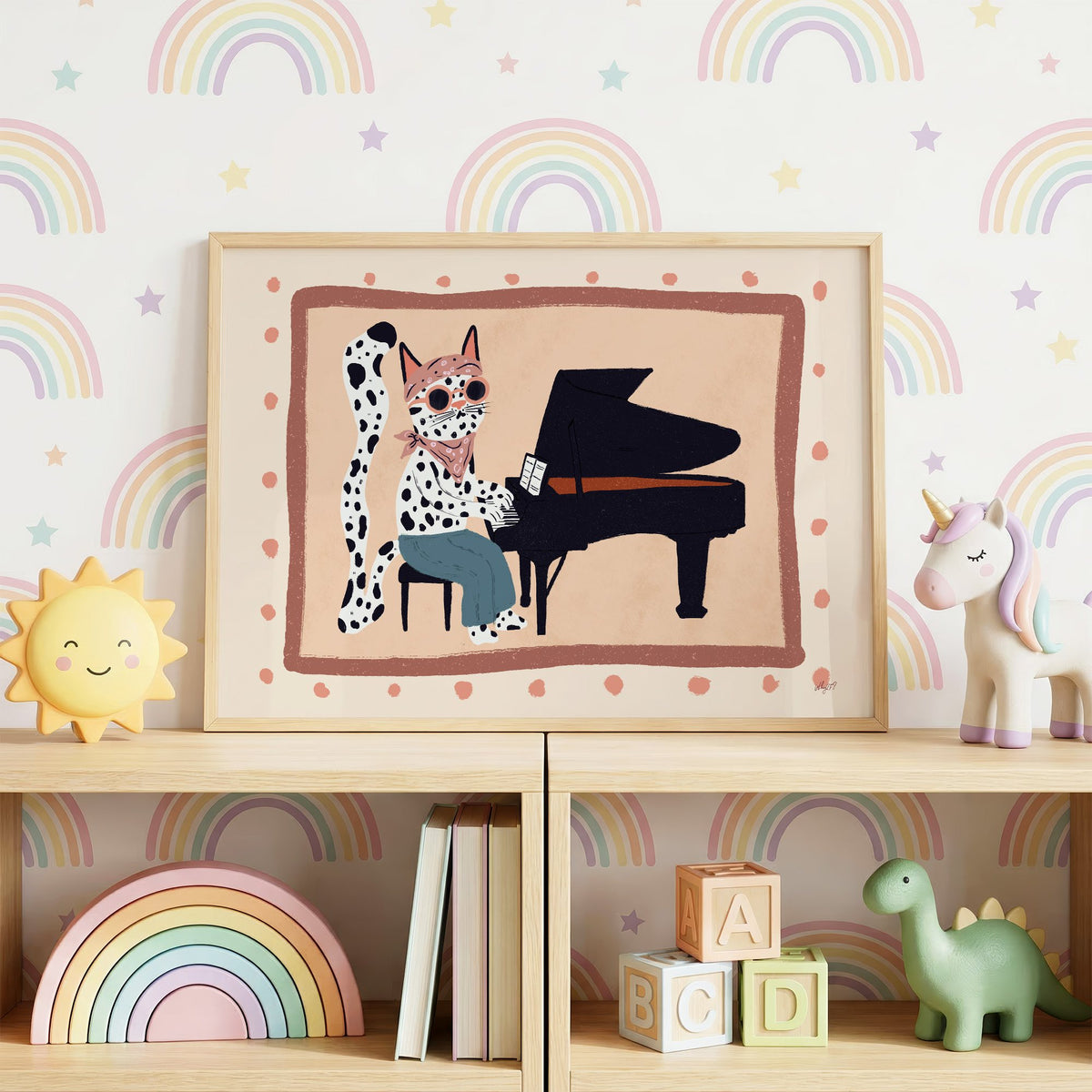 Spotted cat playing grand piano nursery print in an oak frame on a toy shelf against rainbow wallpaper