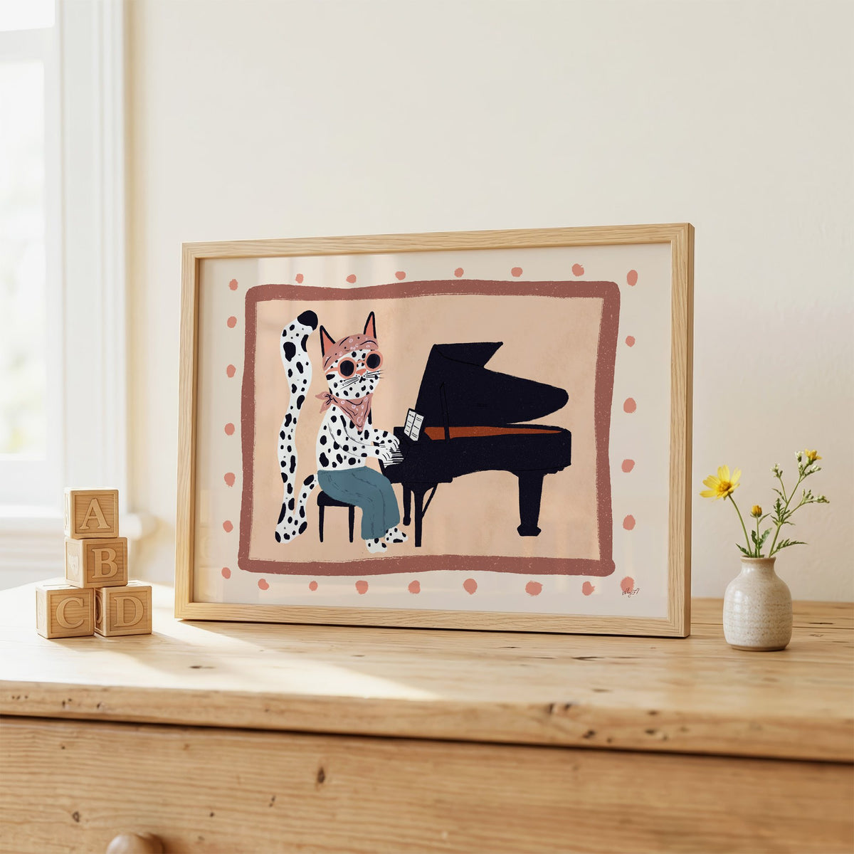 Spotted cat playing grand piano nursery print in an oak frame on a wooden dresser beside ABC blocks