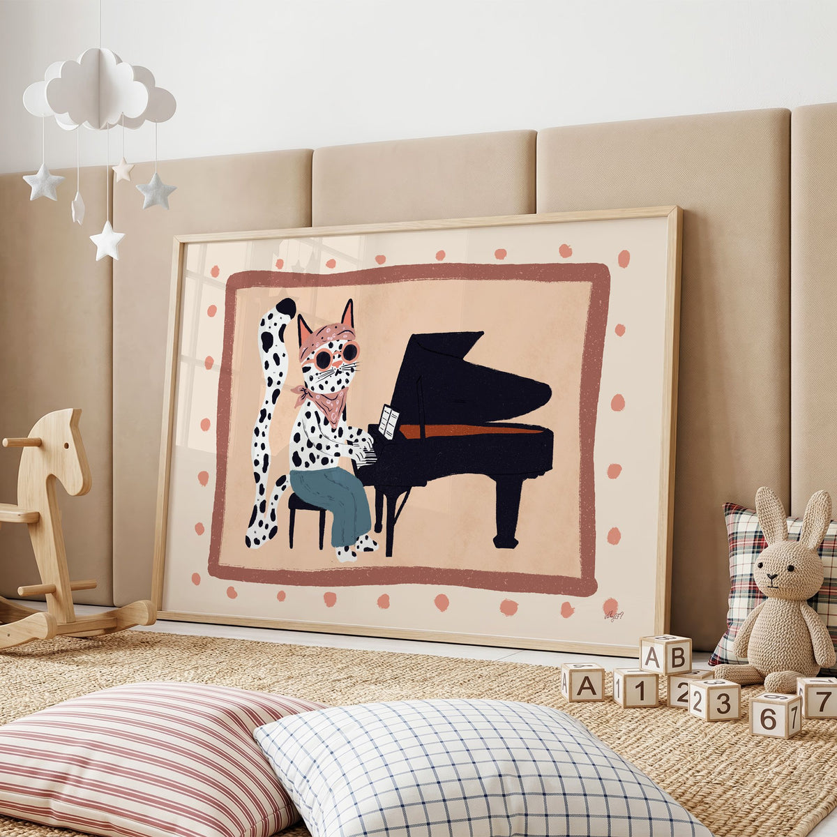 Spotted cat playing grand piano nursery print in an oak frame on a padded wall by a wooden rocking horse
