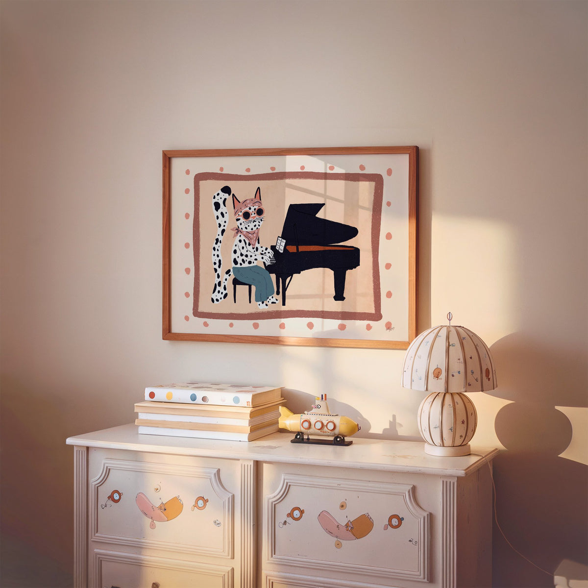 Spotted cat playing grand piano nursery print in a cherry wood frame above a painted dresser and lamp