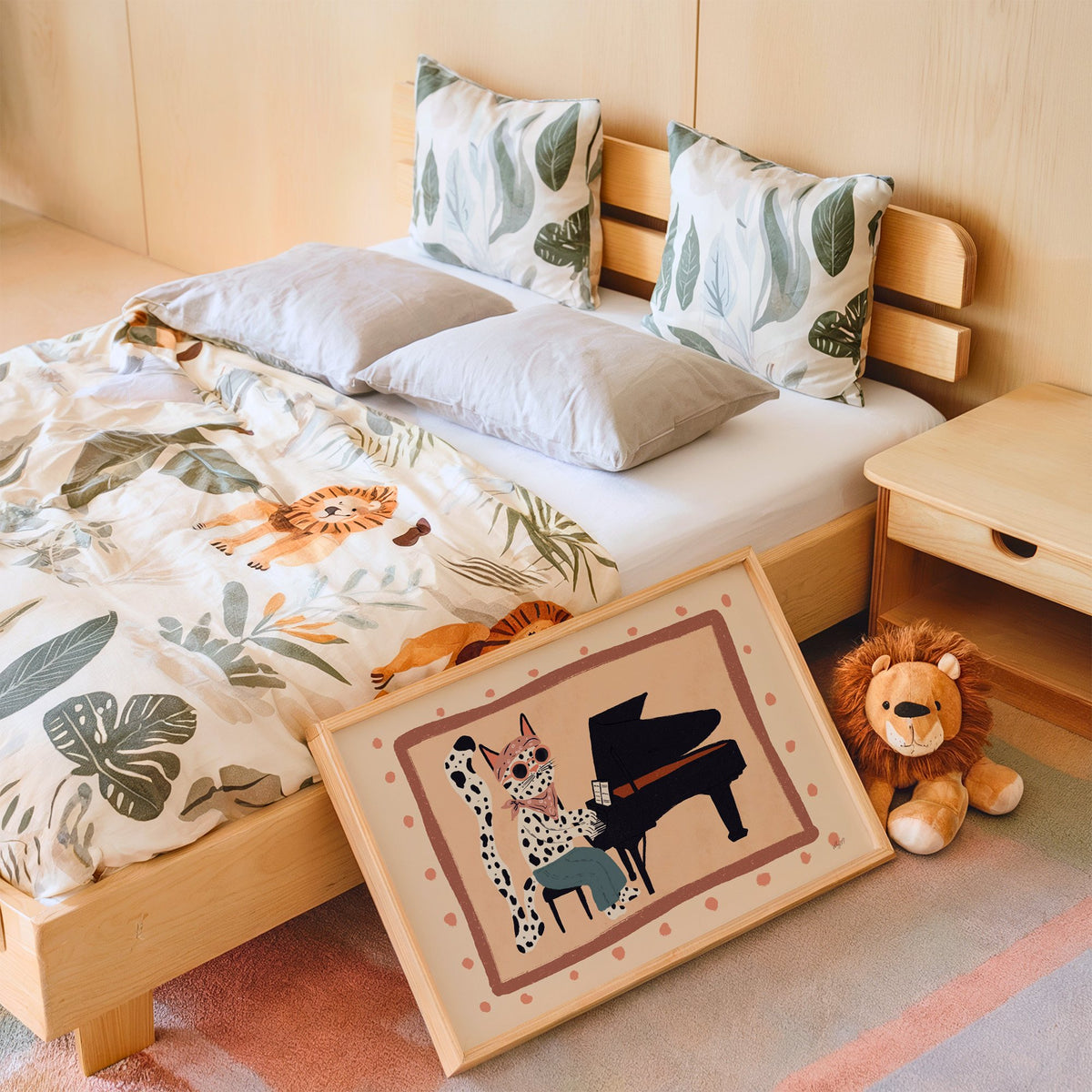 Spotted cat playing grand piano nursery print in an oak frame leaning on a kids bed by a lion plush