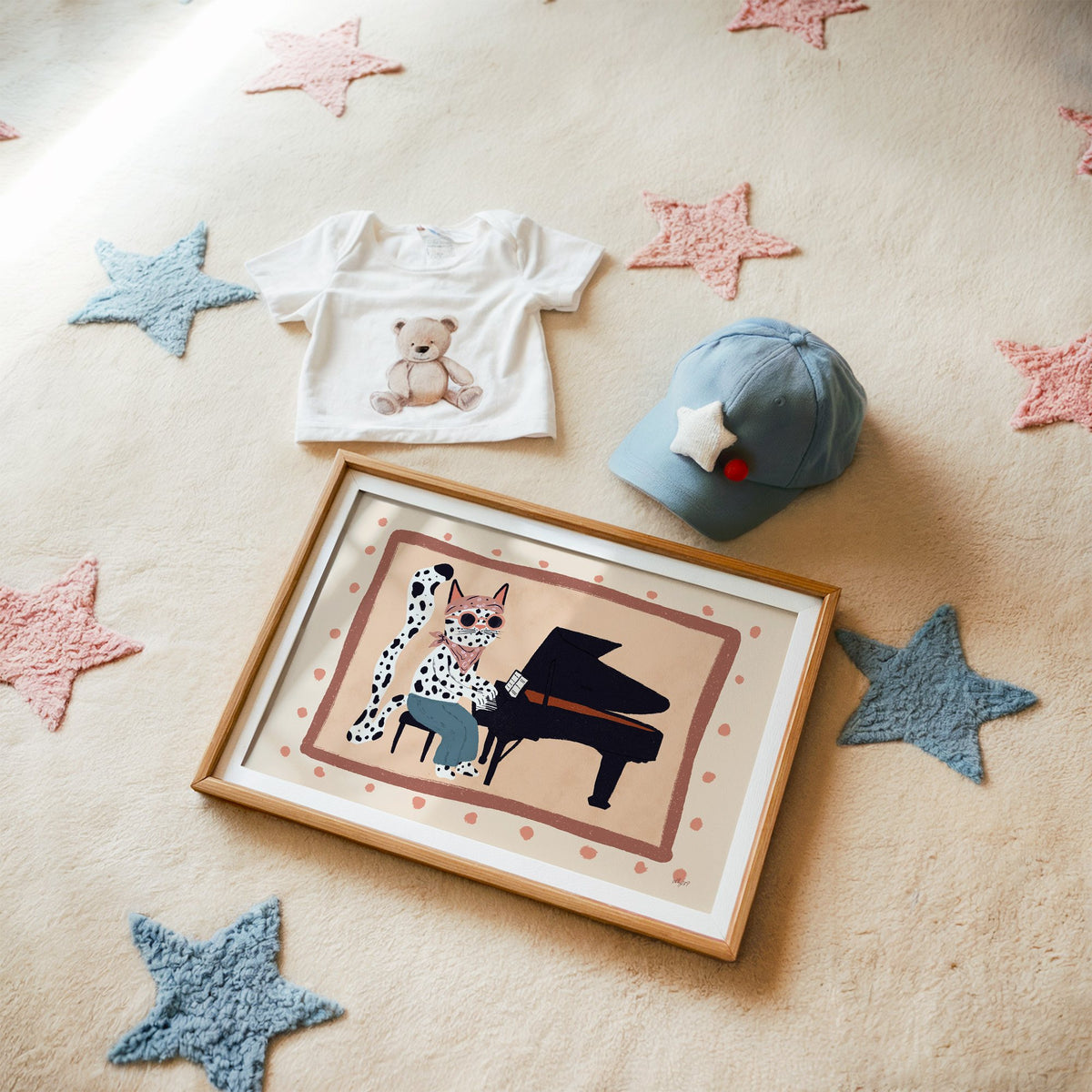 Spotted cat playing grand piano nursery print in a matted oak frame on a star rug with a baby tee