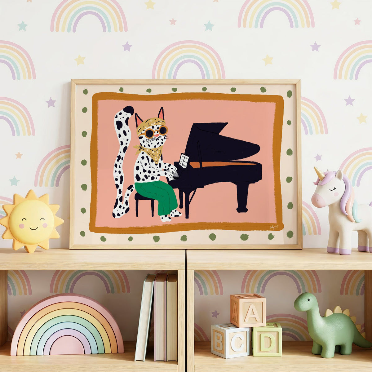 Spotted cat playing grand piano nursery print in an oak frame on a toy shelf against rainbow wallpaper