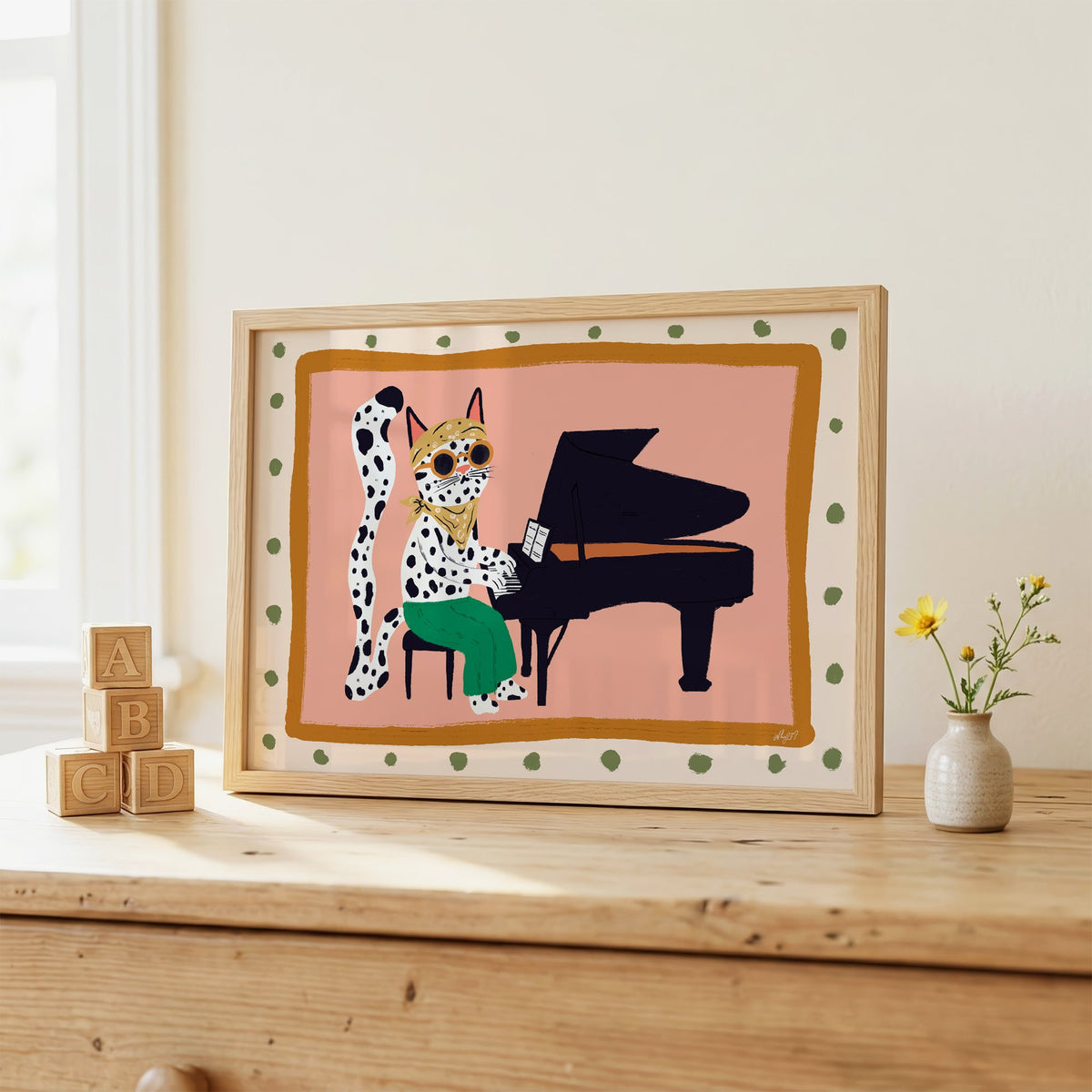 Spotted cat playing grand piano nursery print in an oak frame on a wooden dresser beside ABC blocks