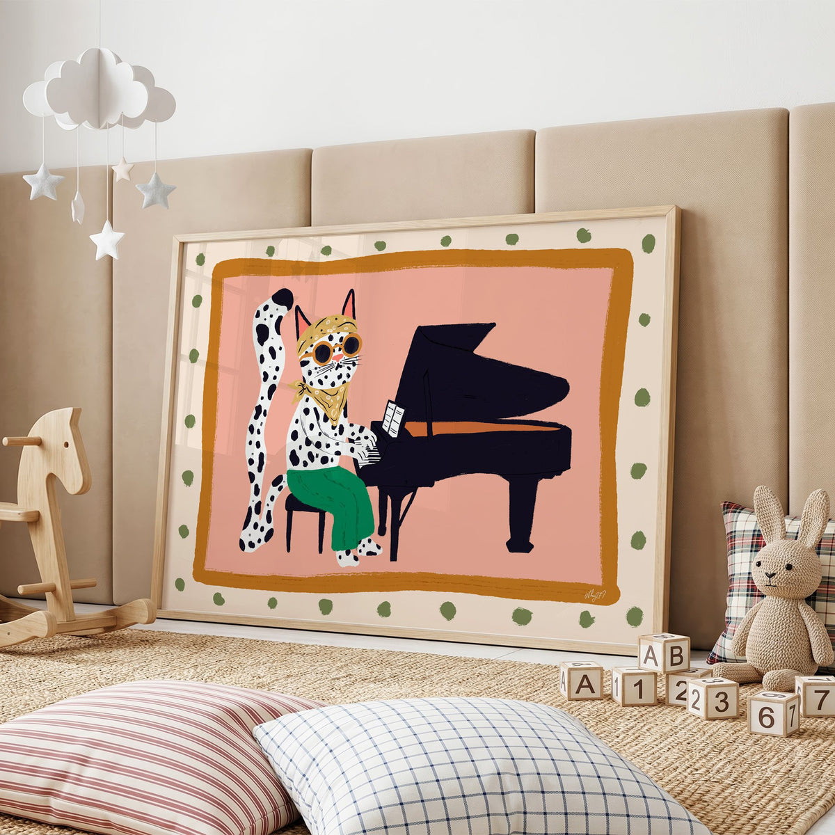 Spotted cat playing grand piano nursery print in an oak frame on a padded wall by a wooden rocking horse