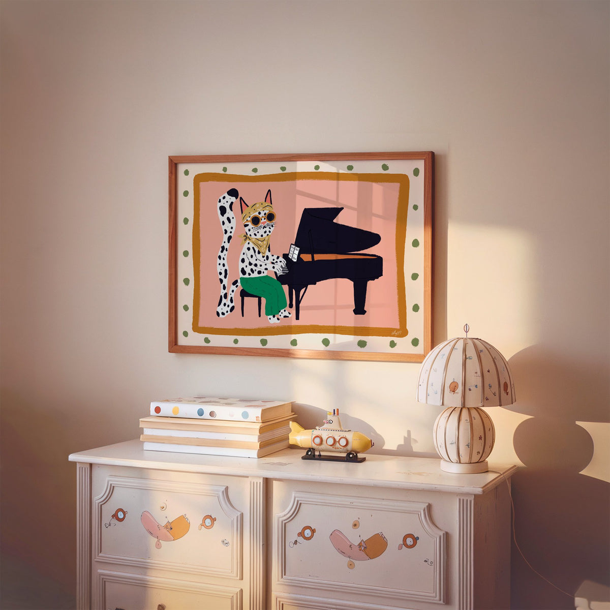 Spotted cat playing grand piano nursery print in a cherry wood frame above a painted dresser and lamp