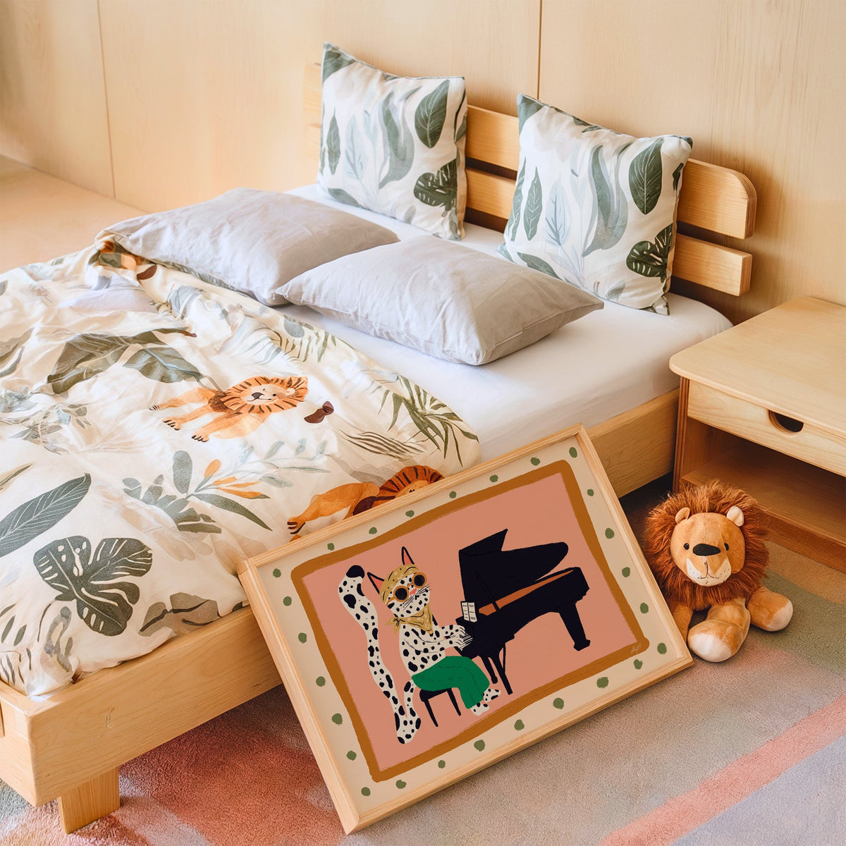 Spotted cat playing grand piano nursery print in an oak frame leaning on a kids bed by a lion plush