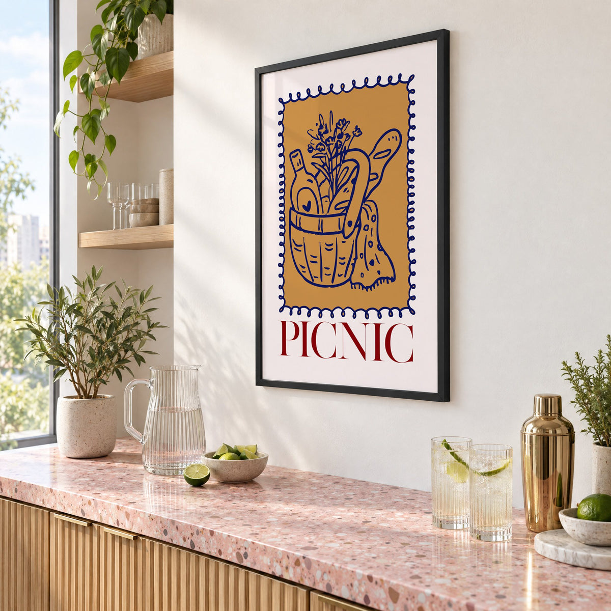 PICNIC basket wine and baguette stamp print in a black frame above a pink terrazzo cocktail counter with limes, seen at an angle
