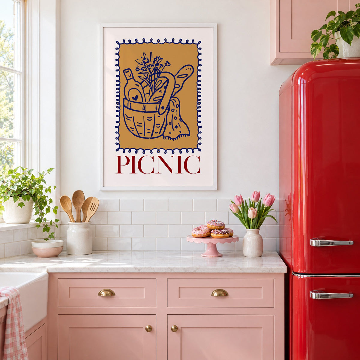 PICNIC basket wine and baguette stamp print in a white frame above pink cabinets beside a red retro fridge