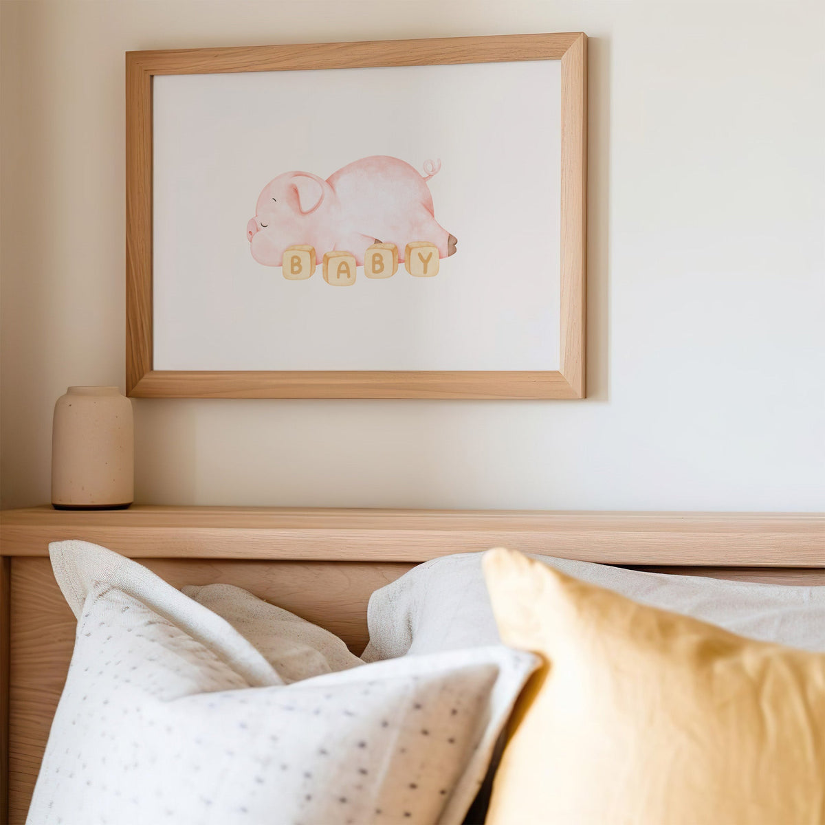 Sleeping pink piglet behind BABY blocks nursery print in an oak frame above a wooden headboard with a mustard pillow