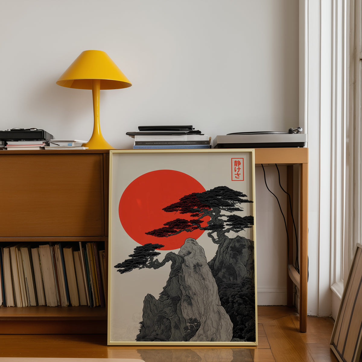 Ink pine cliff with red sun print shown in a gold frame below a teak desk with a yellow lamp