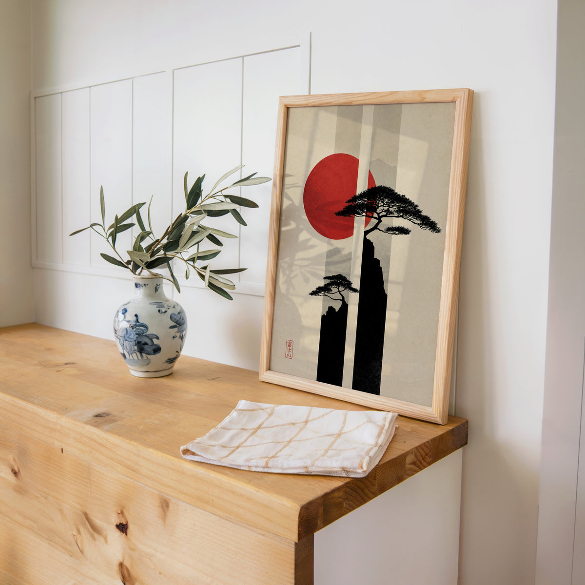 pine cliffs with red sun and stripes print in a pine frame on a wooden counter beside a blue and white porcelain vase