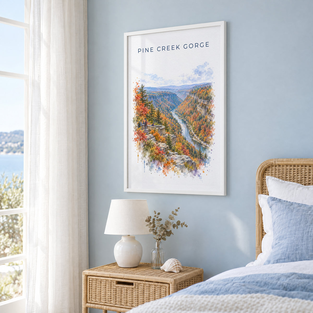 Pine Creek Gorge watercolor print in a white frame on a pale blue wall beside a rattan bed in a coastal bedroom