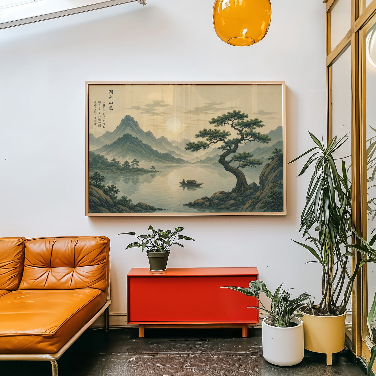Pine tree over a mountain lake at sunrise print in a light wood frame above a red cabinet beside a tan leather daybed