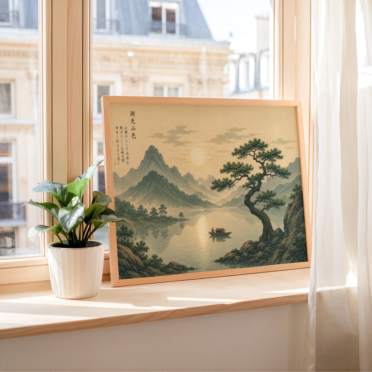 Pine tree over a mountain lake at sunrise print in a light wood frame leaning on a sunny windowsill by sheer curtains