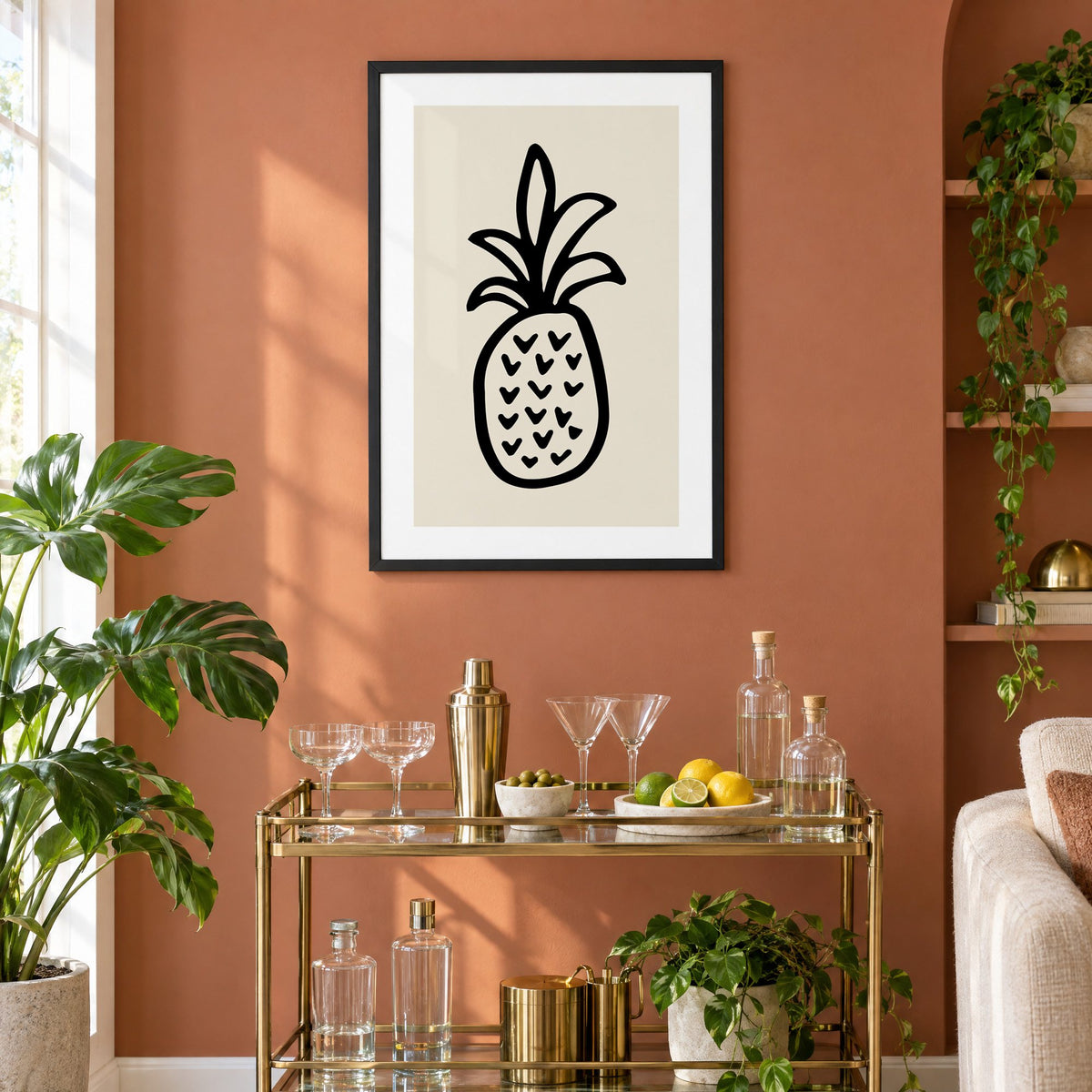 black ink line pineapple beige print in a black frame on a terracotta wall above a brass bar cart with coupes and citrus