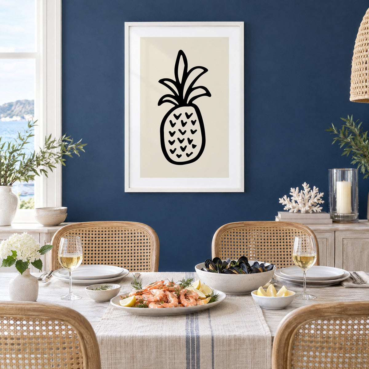 black ink line pineapple beige print in a white frame on a navy wall above a dining table set with shrimp and mussels