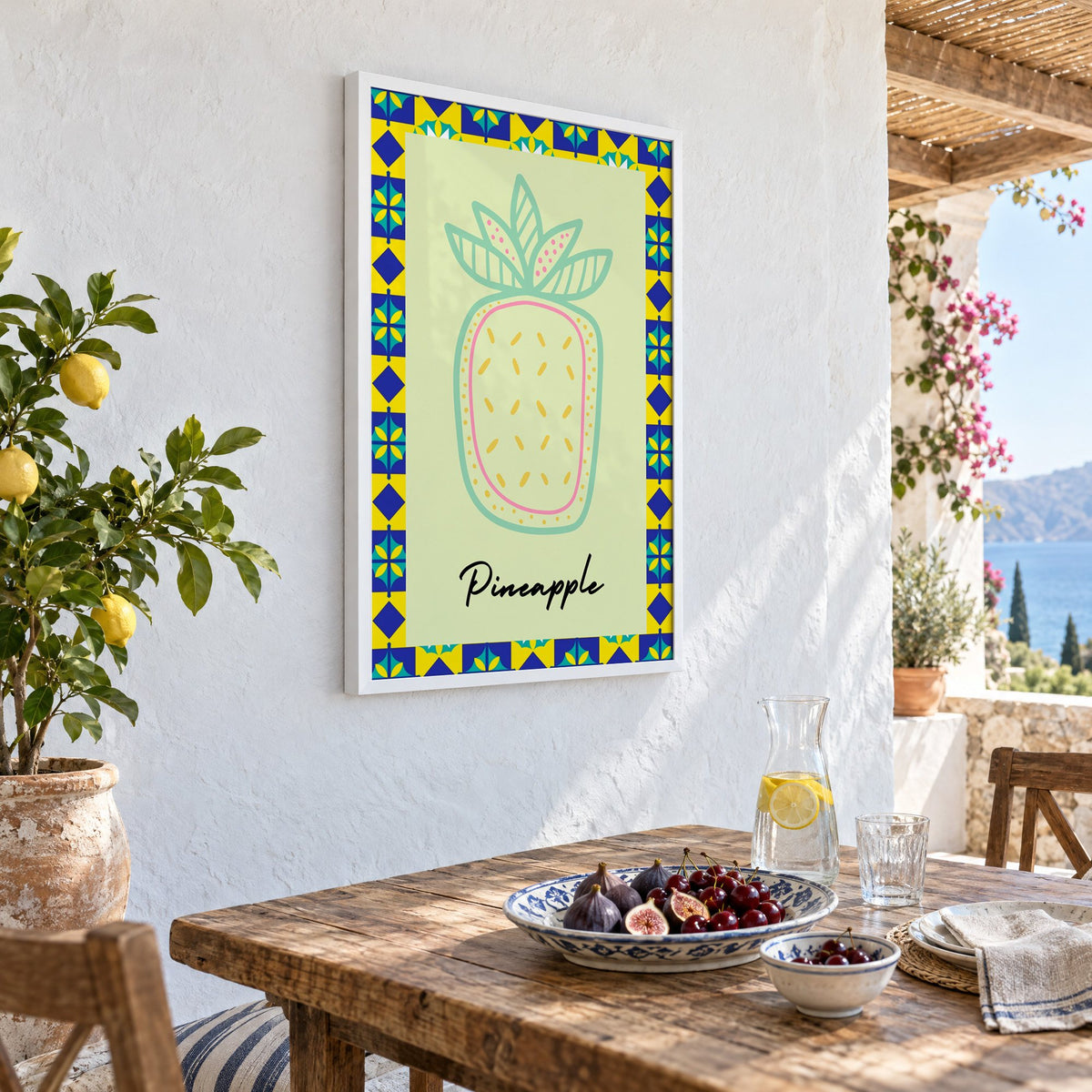 Pineapple mint line-art tile border print in a white frame on a whitewashed terrace wall above a lunch table with figs and cherries, seen at an angle