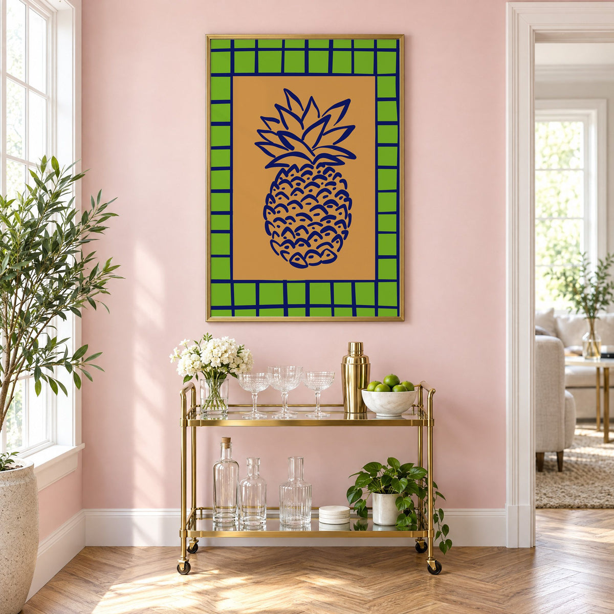 Pineapple navy line on ochre with green grid print in a brass frame on a blush pink wall above a gold bar cart with glassware