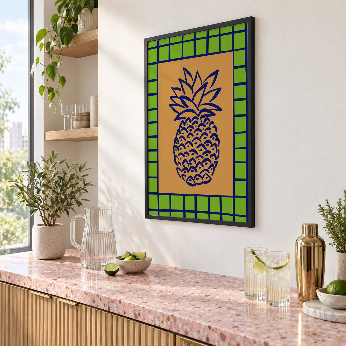 Pineapple navy line on ochre with green grid print in a black frame above a pink terrazzo cocktail counter with limes, seen at an angle