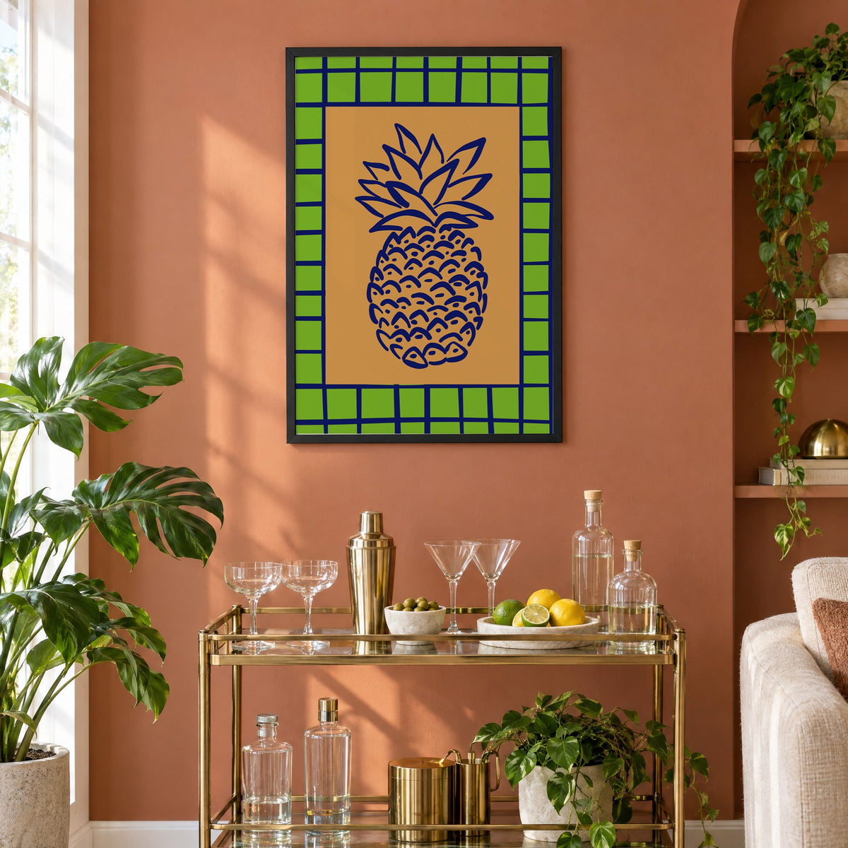 Pineapple navy line on ochre with green grid print in a black frame on a terracotta wall above a brass bar cart with coupes and citrus